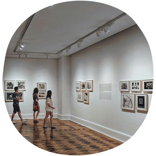 three people walking around a white museum with a glossy brown wood floor