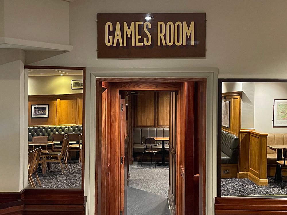 This simply shows the top half of a doorway into their pool room. On either side are two large mirrors that reflect the seating opposite. Above the door is a wooden sign that says games room.
