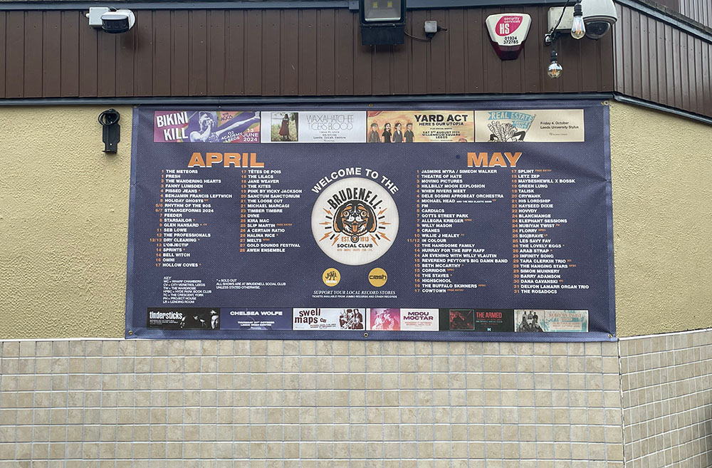 This is a landscape image that shows the large poster that sits outside the venue. In the centre is their logo with an illustrated King Charles Spaniel. On other side of the logo are the montsh April and May. The gigs for those months are shown underneath.