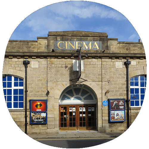 The outside of Cottage road cinema. It shows a building made of yellow bricks with two grand double doors side by side and two windows on either side of the door.