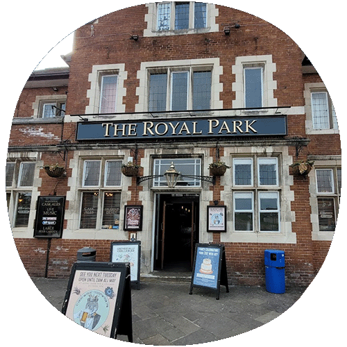 Outside of the pub. Shows the front entrance with a black name banner stating The Royal Park in golden lettering. There are signs outside the pub.