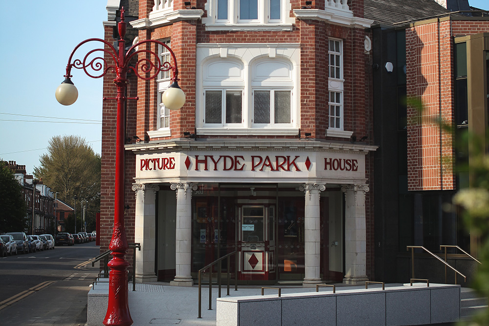 The image is taken from the same angle as the previous elephant photo to show a comparison of the two. It is in daylight and shows the exterior of Hyde Park Picture House. The iconic redd lamppost is on the left side of the image.