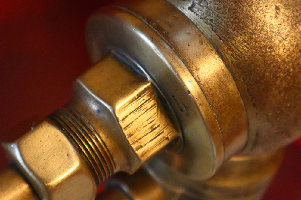 An extreme close up shot of the old brass fire hydrant's shimmering surface. It shows the screws and details of the hydrant over a red background.