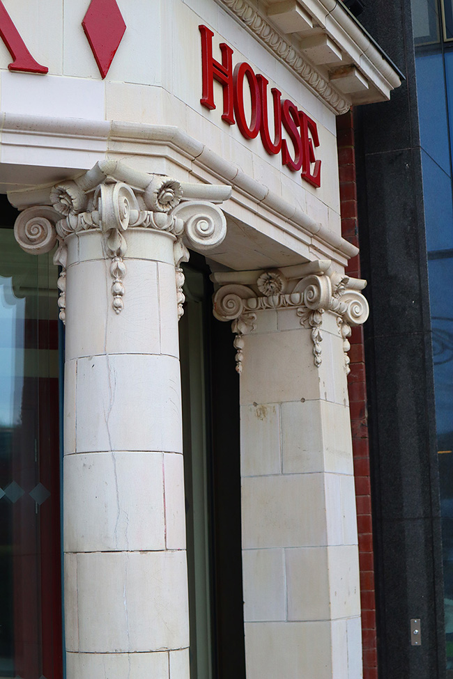 Strong white columns are the primary focus of this image. The columns sit outside Hyde Park Picture House and have roman looking decorations at the top. Above the columns sits the word House in red lettering.
