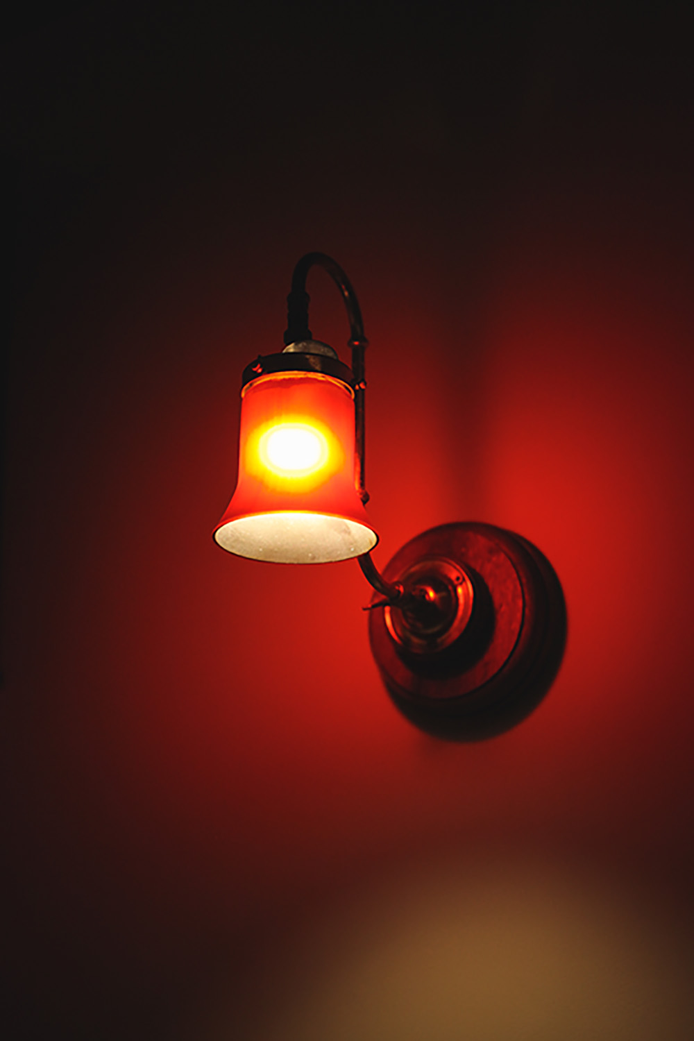 A close up of an old red gaslight. It is a translucent bell shape and disperses red light.