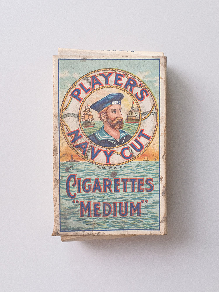 A downward shot of the cigarette packet against a white background. The cigarettes depict the sea in the background with a circle that states the brand. In the middle of this circle is a ginger-haired sailor with a beard and a hat.